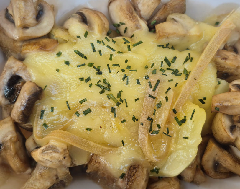 plato de patata con queso raclette fundido y champiñones salteados