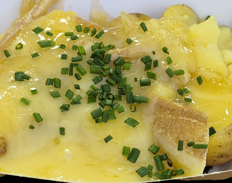 Plato de raclette clásica con patata cocida, queso fundido y encurtidos.