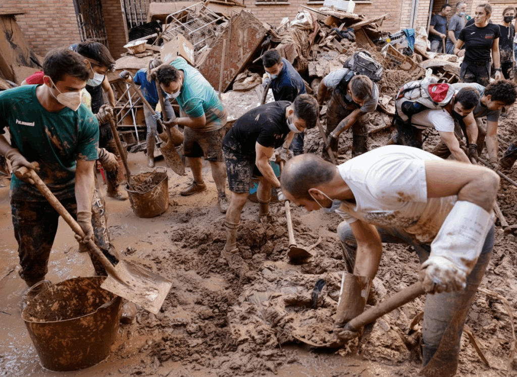 Voluntarios retirando barro y escombros tras la DANA, trabajando con palas en una zona devastada