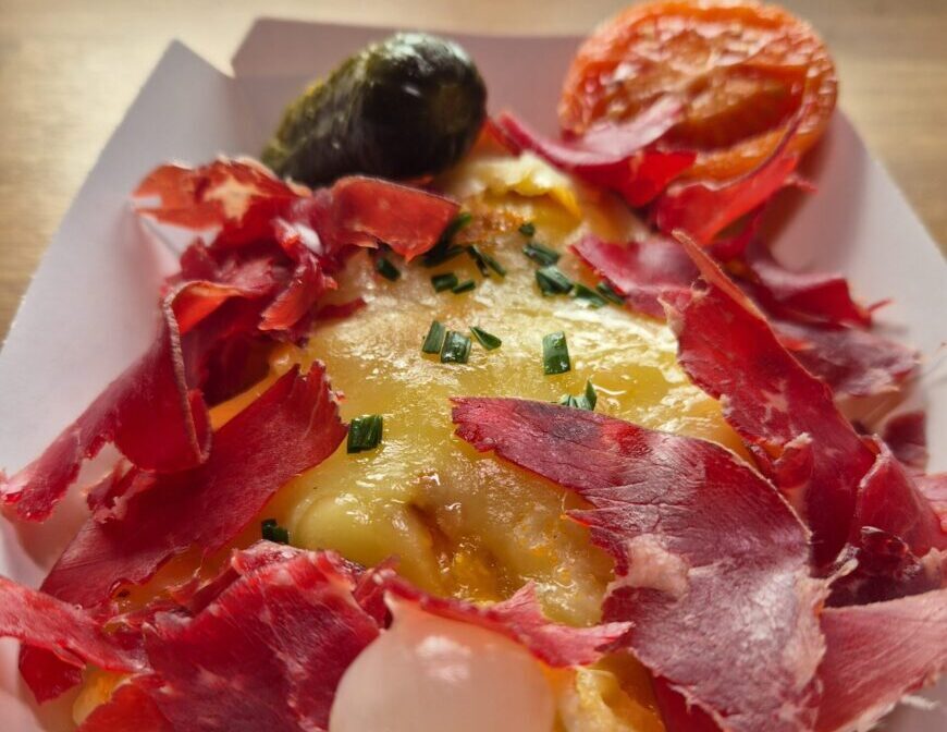 plato de patata con queso raclette fundido y cecina ahumada